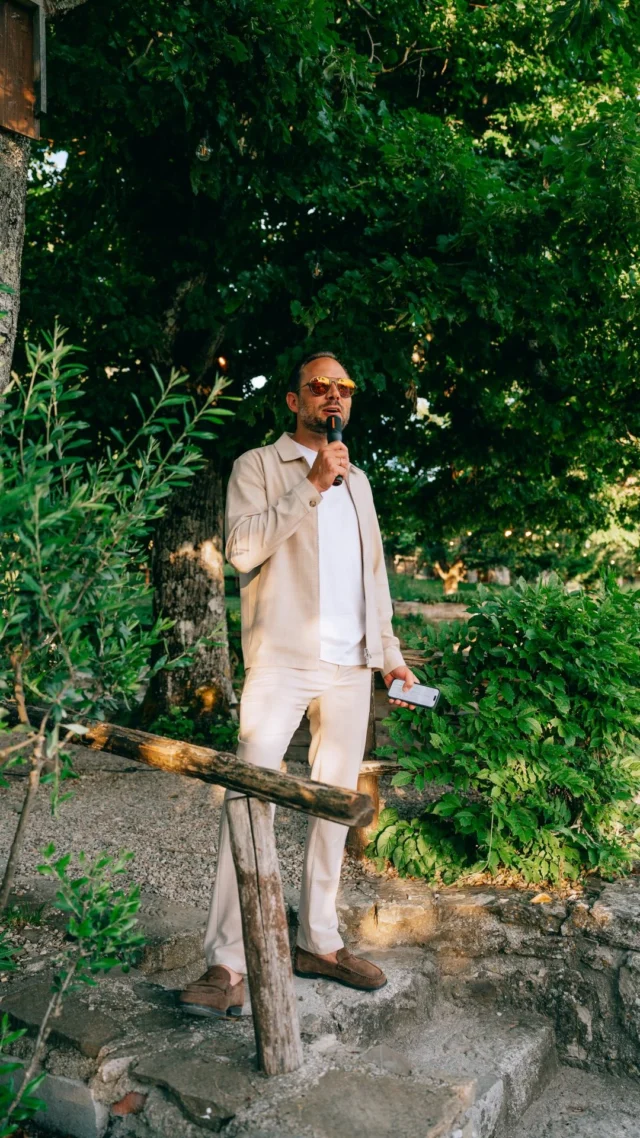 Een presentator met microfoon spreekt de groep toe in een tuin